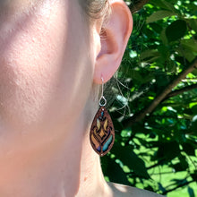 Load image into Gallery viewer, Firefly Forest earrings pictured on a model, wooden teardrop earrings cut with a lace pattern let the rainbow colors of the hand-painted titanium show through