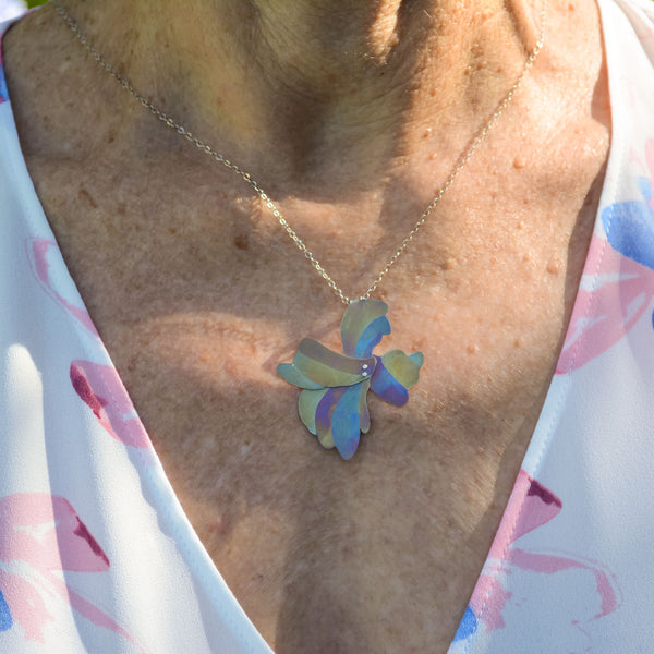 Her Glow at Golden Hour necklace, organic floral shaped pendant hand-painted titanium with yellow, blue, and pink stripes on woman's neck