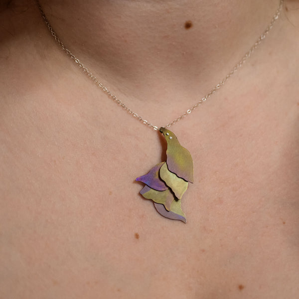 detail of She Wades with Grace Through Changing Tides Necklace on a woman's neckline, a pink and gold hand-painted titanium necklace of layered organic shapes similar to flower petals or feathers