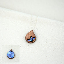 Load image into Gallery viewer, dainty wooden and titanium teardrop shaped necklace with a small floral cutout hand painted in shades of blue