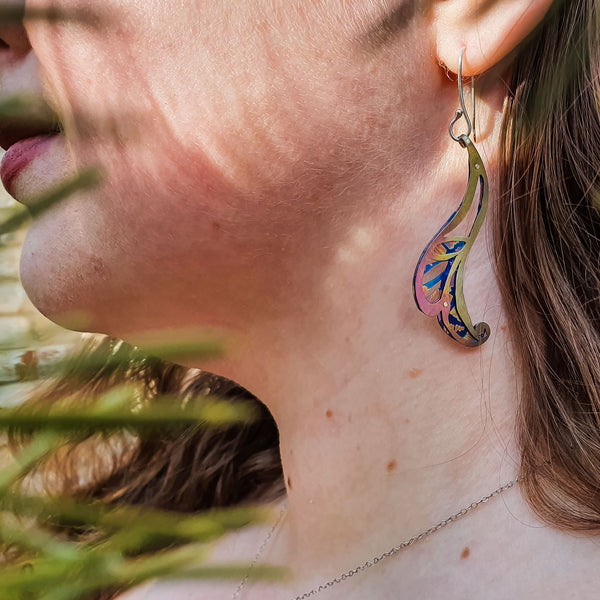 Always Leaf a Little Room for Whimsy earrings, swirly leaf-shaped earrings with little cutouts hand-painted titanium in yellow, pink, and blue modeled on woman's ear