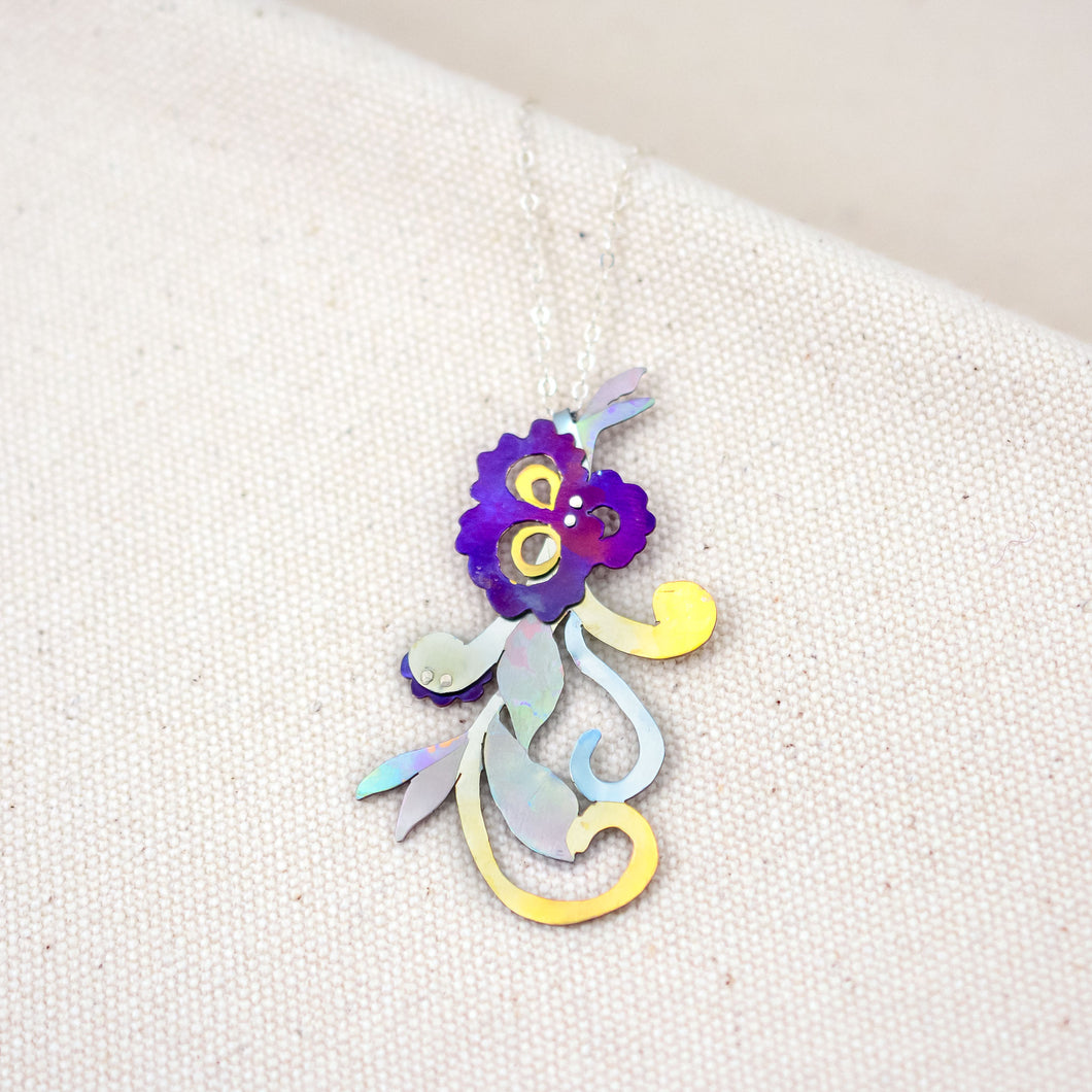 She Will Bloom in a Dark Room necklace, a hand-painted titanium purple flower pendant with curly vines and leaves
