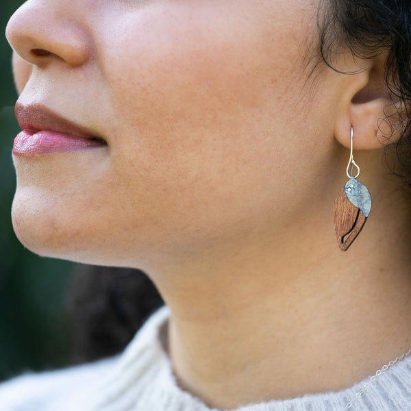 close-up of a woman's lower face wearing The Dew at Dawn earrings, an upside-down teardrop-shaped wooden earrings with a slit down the side and a blue teardrop-shaped piece of titanium riveted on top
