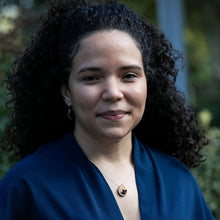 Load image into Gallery viewer, woman smiling and wearing The Freedom to Flourish flower teardrop shaped necklace and a dark blue shirt
