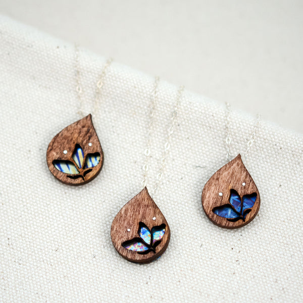 the three different hand painted patterns of The Freedom to Flourish flower necklace, upside down teardrop shaped wooden and titanium necklace with a small flower cutout