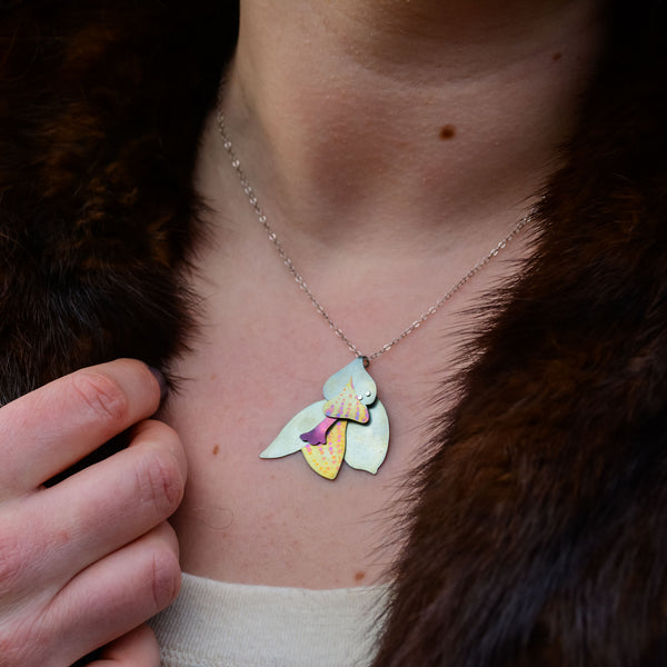The Nectar on Her Neck necklace, flower pendant hand-painted titanium in silver-blue, yellow, and pink on woman's neck