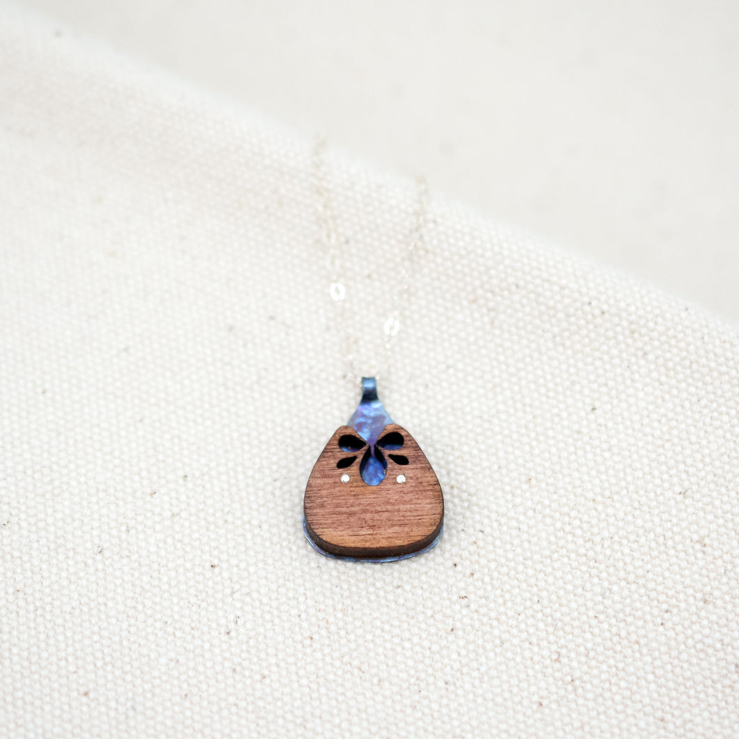The Root of Things necklace, blue speckled titanium shining through a wooden carved rounded triangle