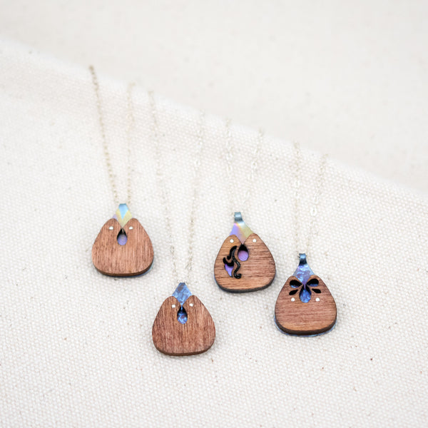 the 4 different variations of the rounded triangular hand painted The Root of Things necklace on a white background.